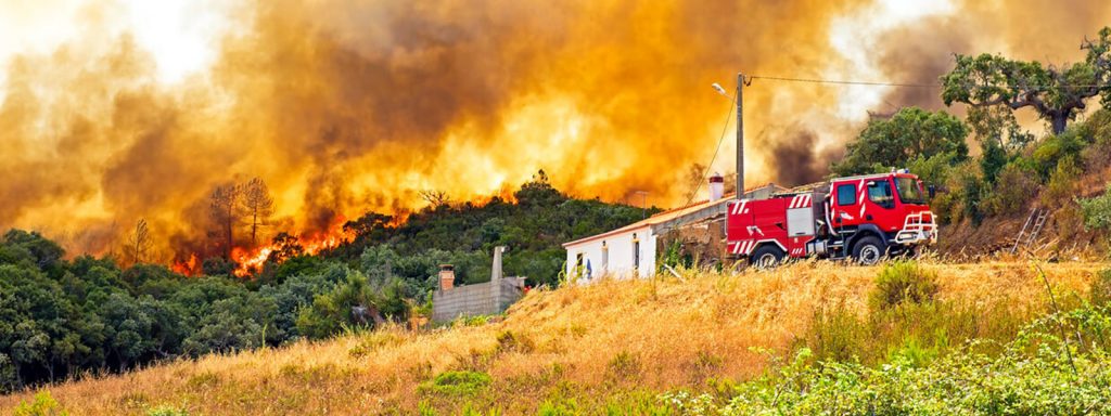 Wildfire burning in hills behind a building and commercial truck