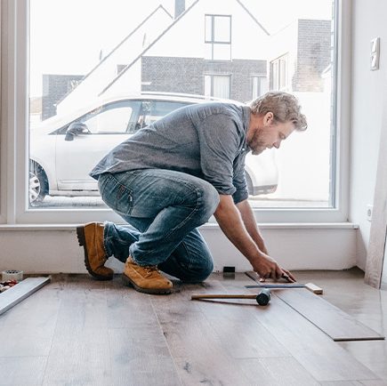 Man installing laminate wood flooring to add value to his home.