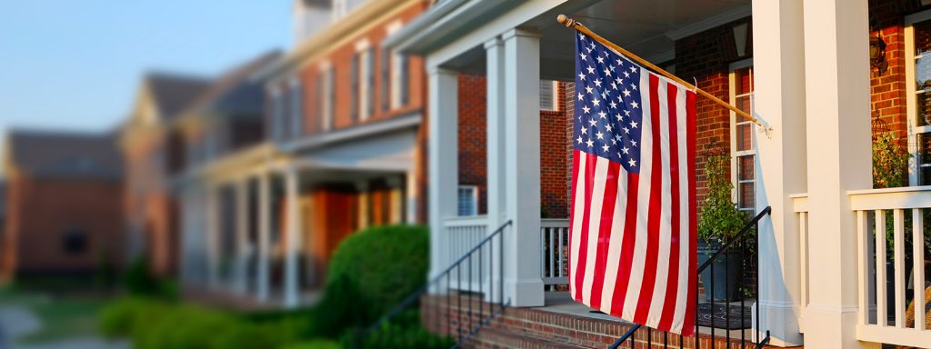 U.S. flag hanging from the front porch of a brick house; lead image for article on facts about va loans